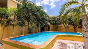 A swimming pool with a curved edge, surrounded by a yellow wall and palm trees.