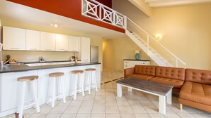 A modern kitchen with white cabinets, a bar area with stools, a brown leather sofa, and a staircase. - Spanish Water Marina Superior Apartment (Jan Thiel)