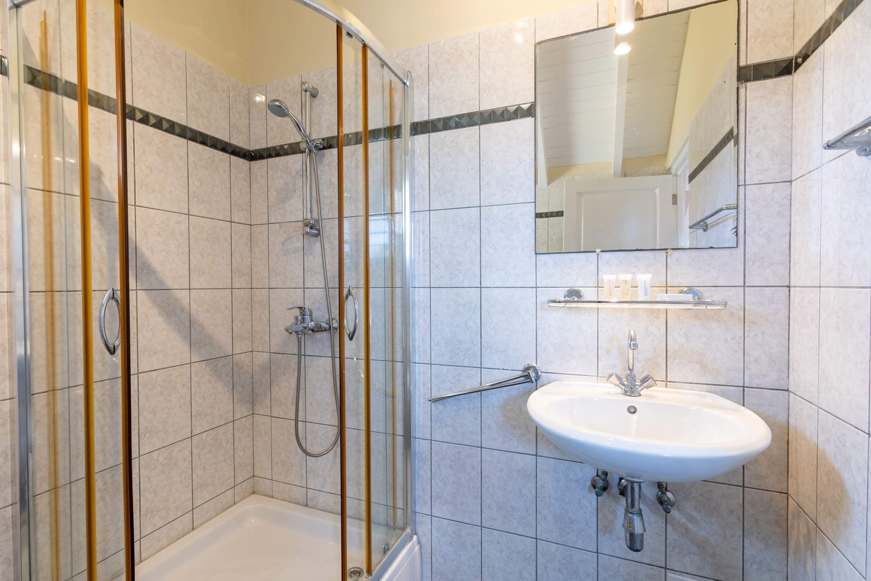Une salle de bain avec une douche à parois de verre, un lavabo blanc et un miroir au-dessus du lavabo.