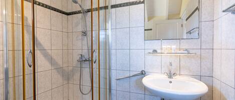 Une salle de bain avec une douche à parois de verre, un lavabo blanc et un miroir au-dessus du lavabo.