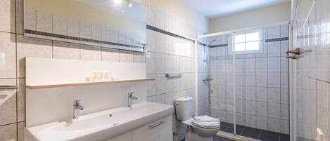 Un baño moderno con un espejo grande, un lavabo, un inodoro y una zona de ducha.