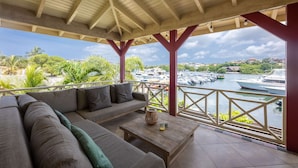A covered outdoor seating area with a sofa and a table, overlooking a marina with boats. - Spanish Water Marina Quad Residences (Jan Thiel)