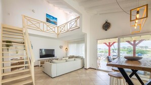 A modern living room with a white sofa, TV, and a wooden staircase. - Spanish Water Marina Quad Residences (Jan Thiel)