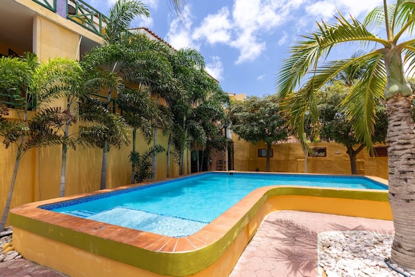 Ein Pool mit geschwungener Kante, umgeben von einer gelben Mauer und Palmen.