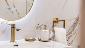 A bathroom with a marble wall, a gold faucet, a white sink, a gold soap dispenser, and a towel rack. - Lemair Luxury Apartments Kozani Deluxe Double Room (Kozani)