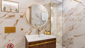 Un baño con pared de mármol, un espejo redondo, un lavamanos y una ducha.