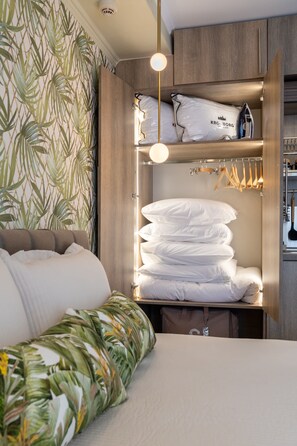 A neatly organized hotel room with a bed, a wardrobe with hanging clothes, and a shelf with pillows and bags. - Lemair Luxury Apartments Kozani Deluxe Apartment (Kozani)