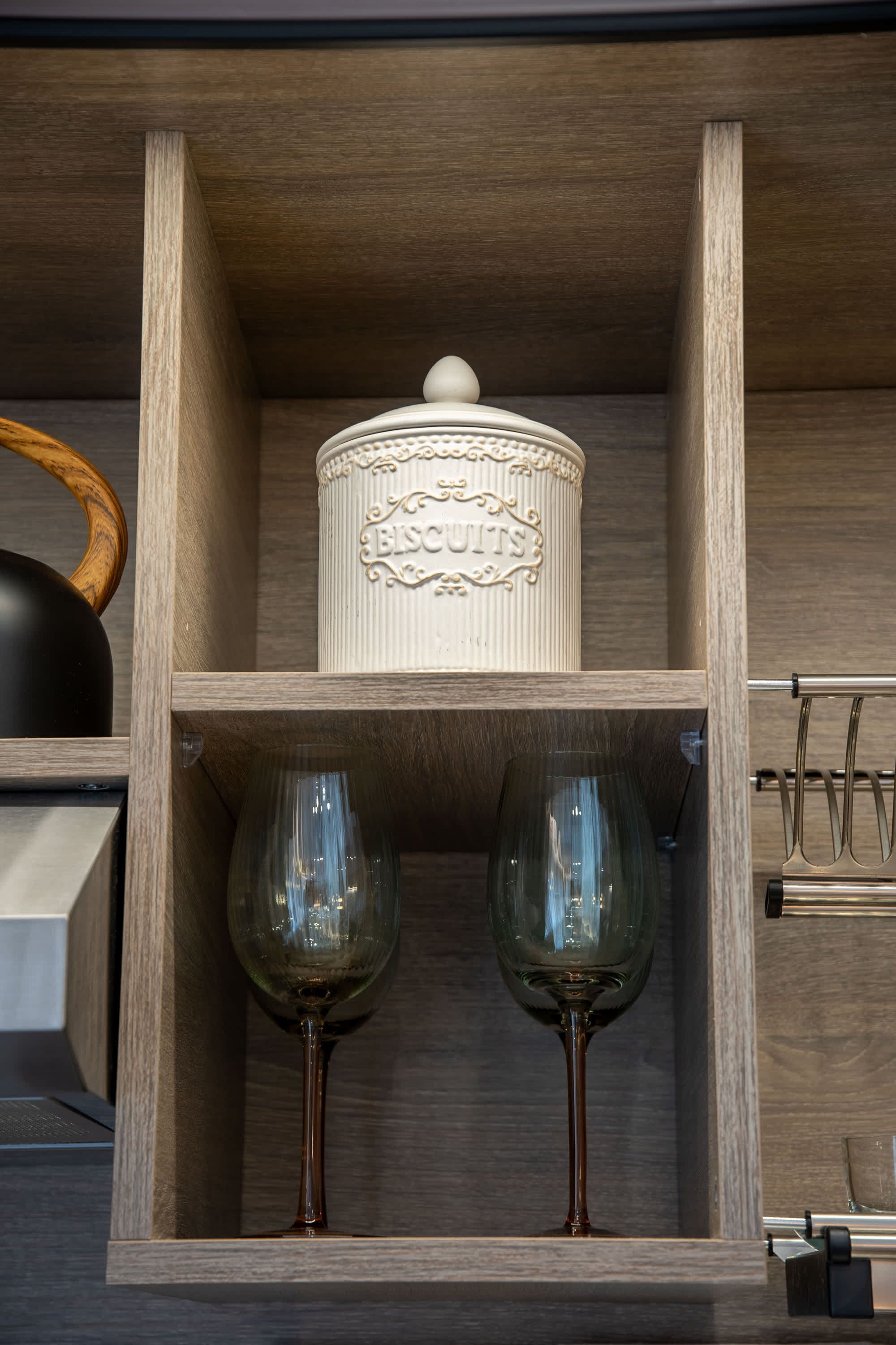 Um armário de madeira com um recipiente decorativo com a etiqueta 'EISCUITS' e dois copos de vinho.