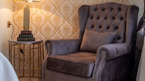 A tufted armchair with a cushion, a small side table with a lamp, and a patterned wallpaper. - Lemair Luxury Aprtmnts Kozani Deluxe Junior Suite (Kozani)