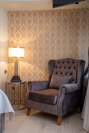 A tufted armchair with a cushion, a small side table with a lamp, and a patterned wallpaper. - Lemair Luxury Aprtmnts Kozani Deluxe Junior Suite (Kozani)