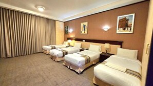 Quarto de hotel com três camas, uma janela grande com cortinas, uma TV fixada na parede e um quadro.