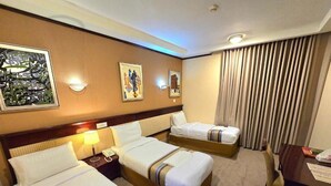Quarto de hotel com duas camas, uma escrivaninha, uma cadeira e uma janela com cortinas.
