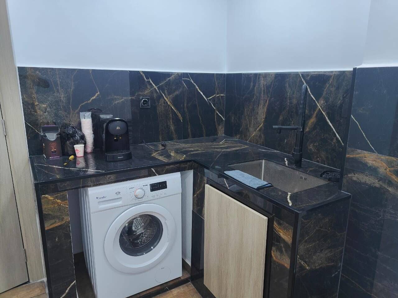A compact kitchen with a washing machine, a coffee maker, and a sink.