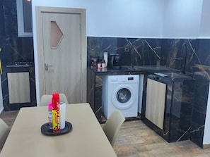 Une cuisine compacte équipée d’un lave-linge, d’une machine à café et d’un coin repas avec une table et des chaises.