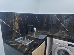 A compact kitchen with a washing machine, a sink, and a marble backsplash. - Luxury apartment for your stay in Skikda (Filfila)