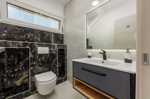 A modern bathroom with a toilet, vanity, and large mirror. - Villa Weiss 2 (Vir)
