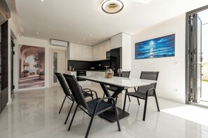 A modern kitchen with white cabinets, a dining table with chairs, and a large painting on the wall. - Villa Weiss 2 (Vir)