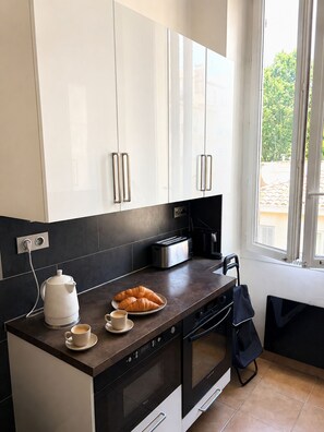 A modern kitchen with white cabinets, a dark countertop, a toaster, a kettle, and a plate of croissants. - L'appartement Consolat (Marseille)