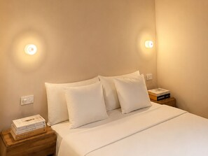 A neatly made bed with white bedding and pillows, a wooden nightstand with books, and wall-mounted light fixtures. - L'appartement Consolat (Marseille)