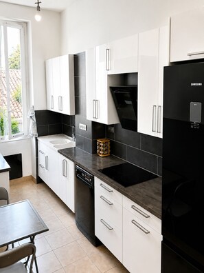 A modern kitchen with white cabinets, a black refrigerator, and a built-in oven. - L'appartement Consolat (Marseille)