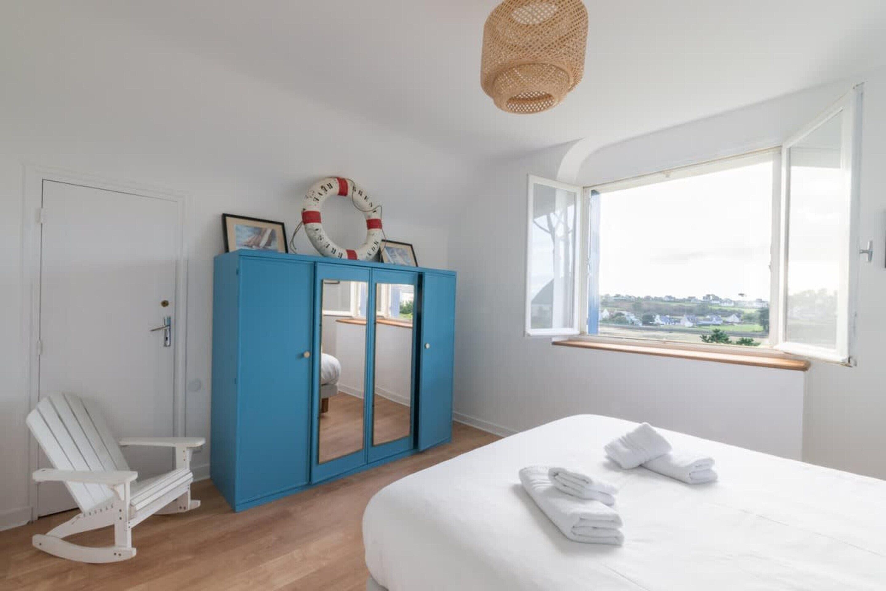 Ein Schlafzimmer mit einem Bett, einem blauen Kleiderschrank, einem weißen Schaukelstuhl und einem Fenster mit Blick.