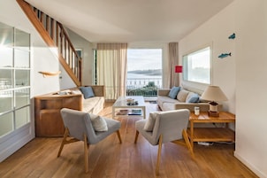 Una sala de estar moderna con una escalera, un conjunto de sofás, una mesa de centro y vistas a una masa de agua.