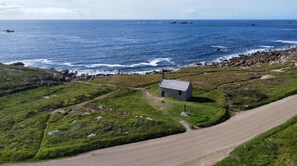 Eine Küstenlandschaft mit einem kleinen Steinhäuschen, einem Feldweg und dem Meer.