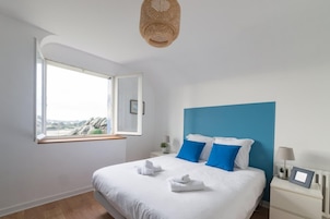 Un dormitorio con cama, ventana, mesita de noche y lámpara colgante.