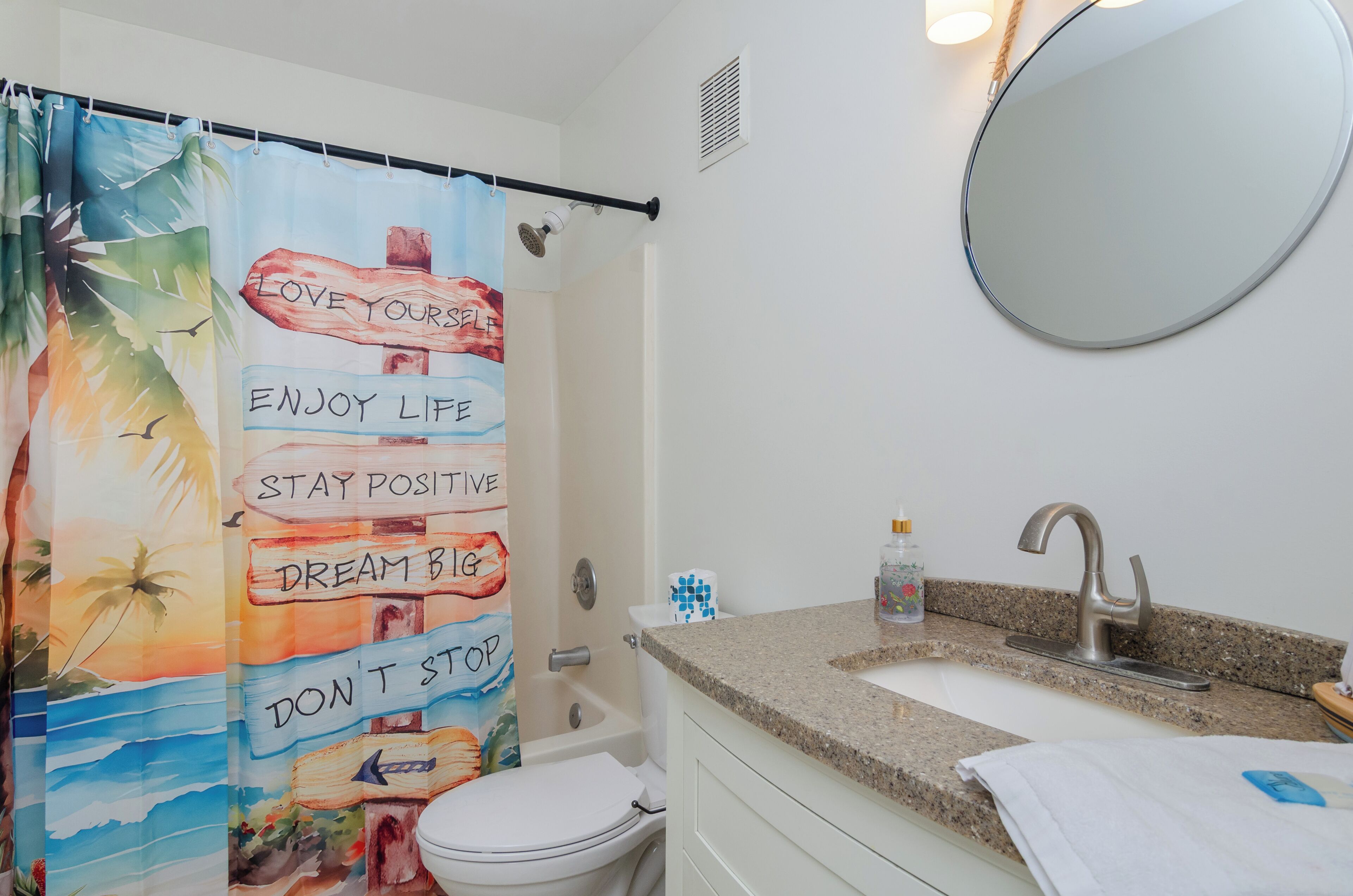 A bathroom with a shower curtain featuring motivational phrases, a sink with a faucet, and a mirror.
