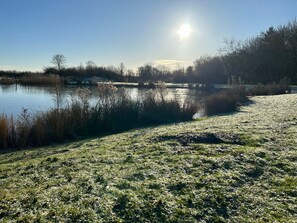 Eine friedliche Seenlandschaft mit blauem Himmel, ruhigem Wasser und mit Reif bedecktem Gras.
