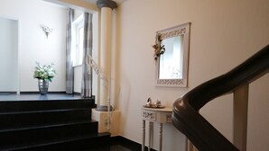 Eine glatte schwarze Treppe führt zu einer Empore mit einer weißen Säule, einem kleinen Tisch mit Dekoration und einem Spiegel an der Wand.