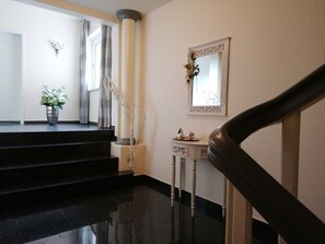 Eine glatte schwarze Treppe führt zu einer Empore mit einer weißen Säule, einem kleinen Tisch mit Dekoration und einem Spiegel an der Wand.