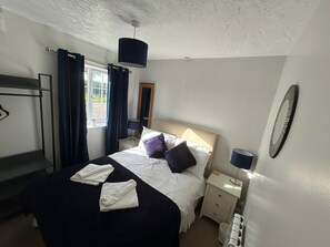 Ein Schlafzimmer mit Bett, Nachttischen, einer Hängelampe, einem Spiegel und einem Fenster mit Vorhängen.