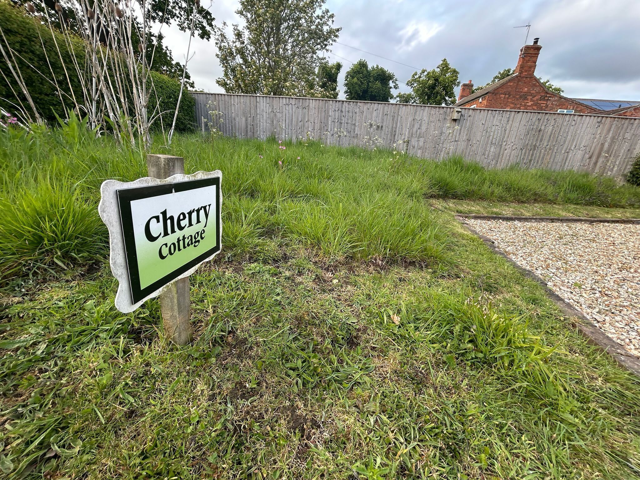 A sign for Cherry Cottage with a grassy area and a wooden fence in the background.