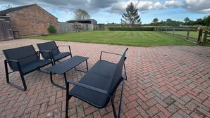 An outdoor patio with black metal furniture, a brick floor, and a view of a grassy yard with trees and a wooden fence.