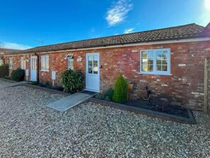 A brick building with a gravel driveway, a small garden, and a clear blue sky. - Private Fishing Lake Cottage - Pet Friendly w/ (Burgh le Marsh)