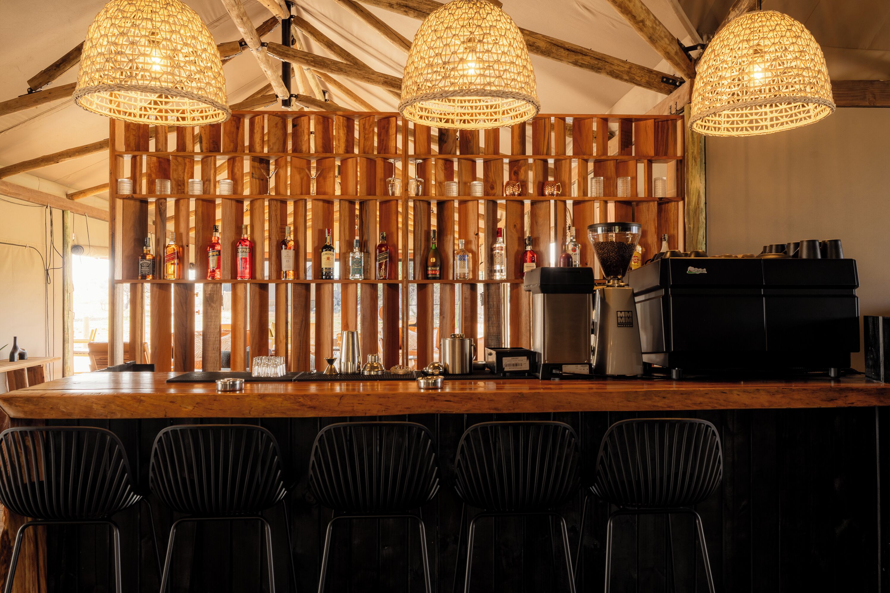 A bar area with wooden shelves, bar stools, and a coffee machine.