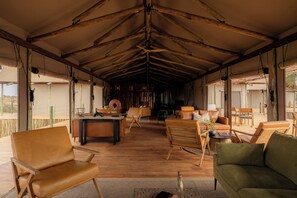 A spacious interior with a high ceiling and wooden beams, furnished with leather sofas and chairs, and a central table. - Kuona Serengeti (Serengeti)
