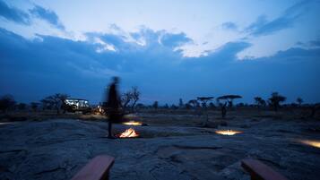 A campsite with a fire, a vehicle, and a person walking.