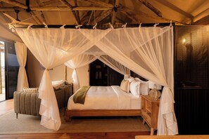 A bedroom with a four-poster canopy bed, a wooden headboard, and a bedside table with a lamp. - Kuona Serengeti (Serengeti)