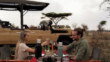 Une table à manger avec de la nourriture et des boissons, un véhicule en arrière-plan et une tente.