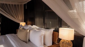 Ein Schlafzimmer mit einem Bett, Kissen, einer Nachttischlampe und einem Fenster mit durchsichtigen Vorhängen.