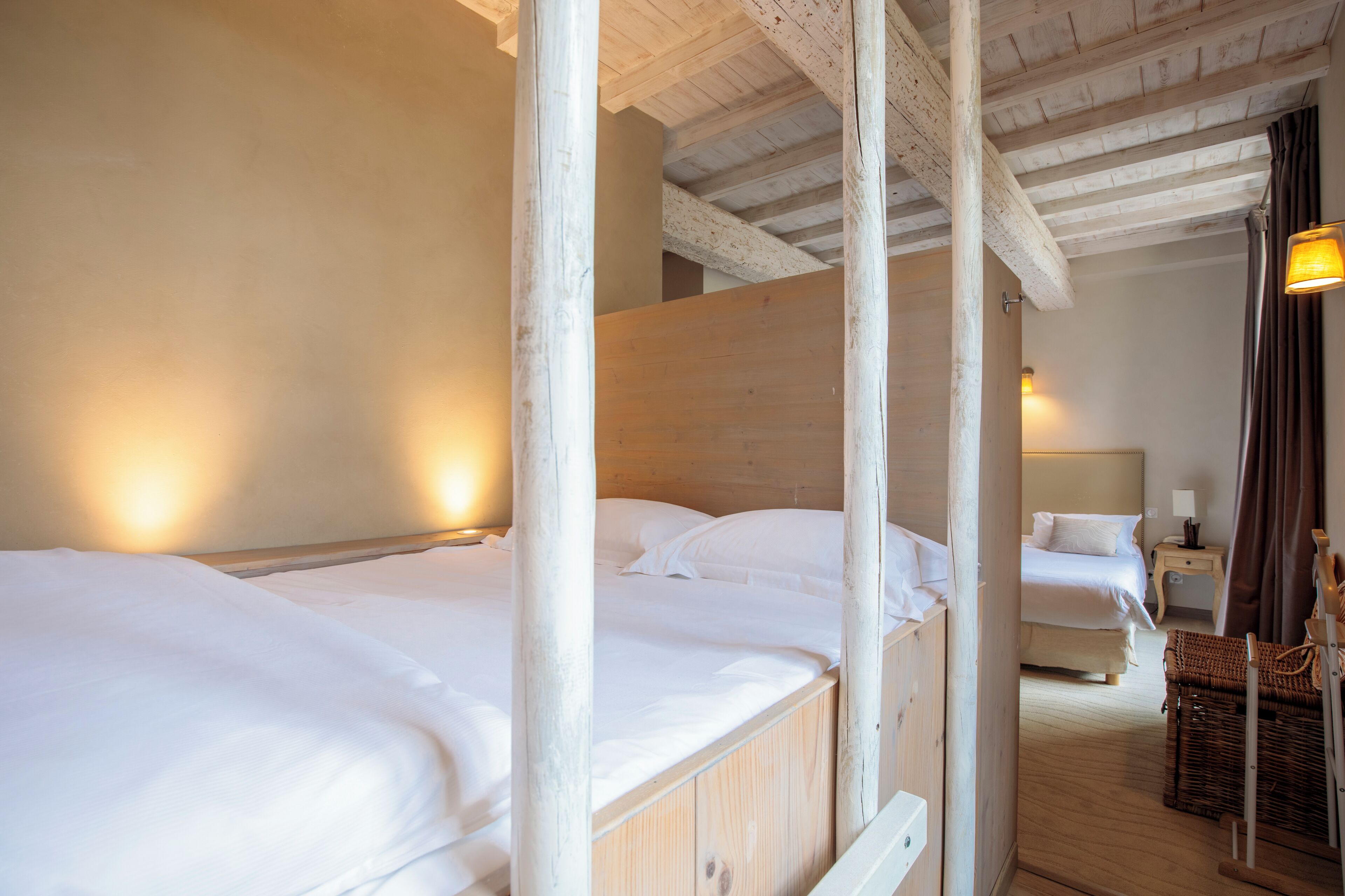 A wooden cabin-style room with two beds, a nightstand, a lamp, and a wicker chair.