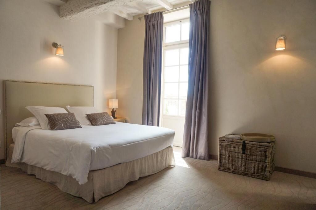 A bedroom with a large bed, two bedside lamps, a wicker basket, and a window with curtains.