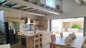 A modern kitchen with a central island, pendant lighting, and a dining area with a table and chairs. - Boutique Hôtel La Villa Montesquieu (Laudun)