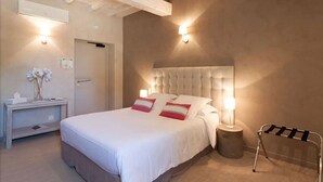 A hotel room with a large bed, bedside lamps, a nightstand, a towel rack, and a door. - Boutique Hôtel La Villa Montesquieu (Laudun)