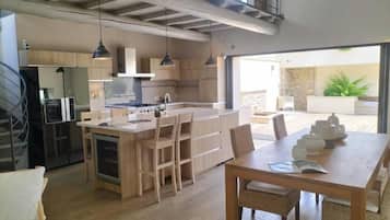 A modern kitchen with a central island, wooden cabinets, pendant lighting, and a dining area with a table and chairs.