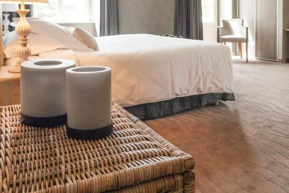 Habitación de hotel con una cama grande, una mesita de mimbre, una lámpara y vistas al exterior a través de la ventana.
