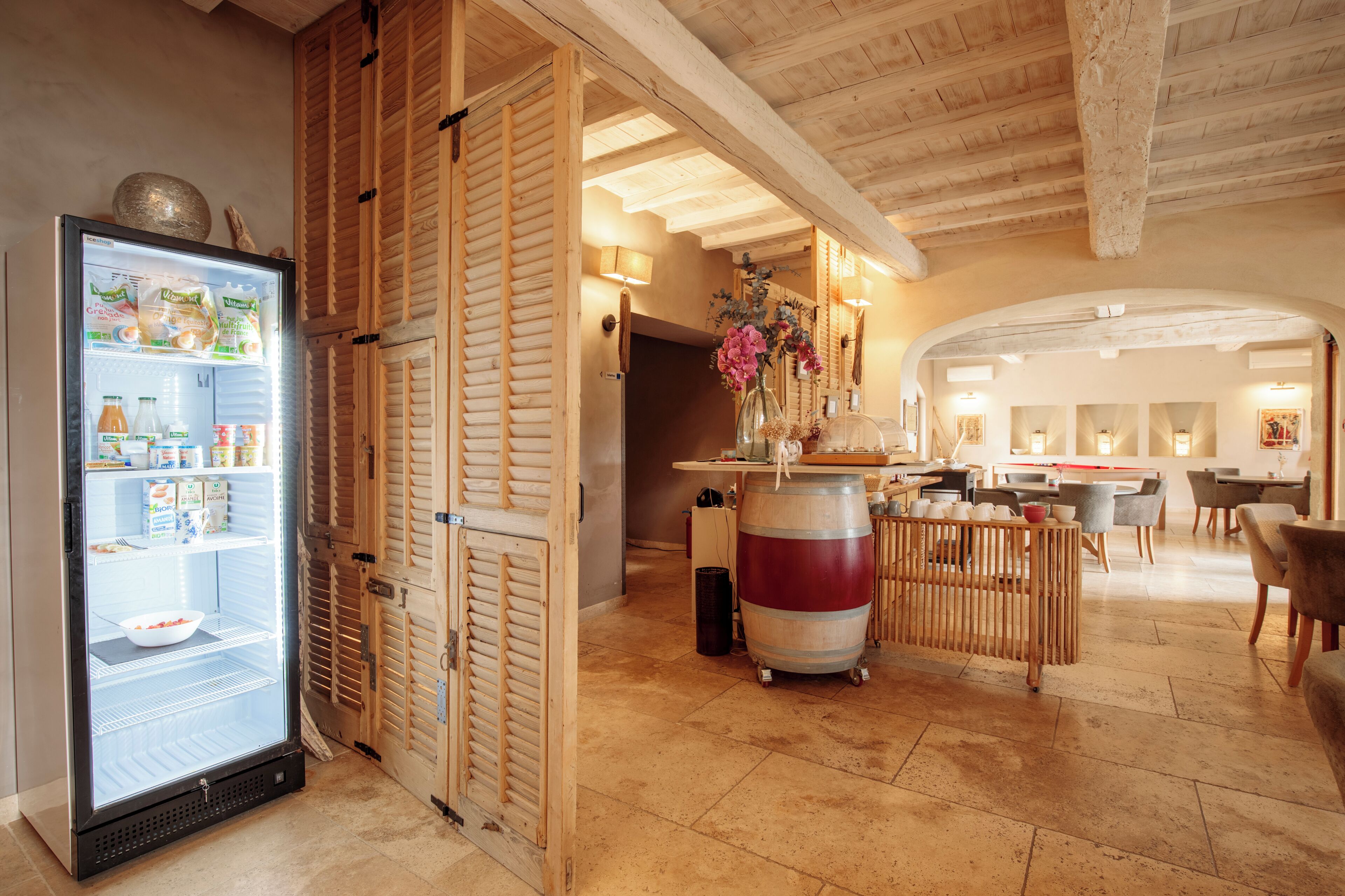 Habitación de hotel con minibar, contraventanas de madera, un barril grande y una zona de comedor con mesas y sillas.