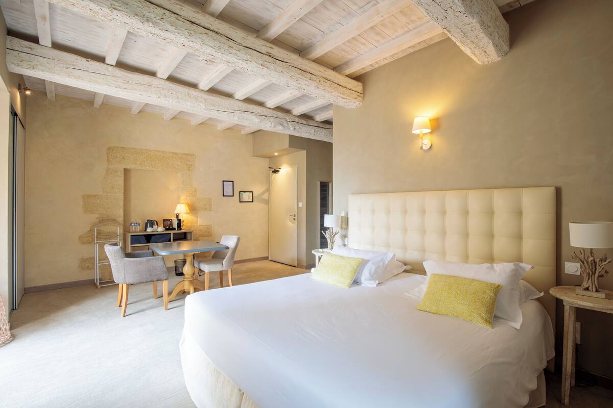 Habitación de hotel con una cama grande, un escritorio con sillas, una mesita con lámpara y una luz en la pared.